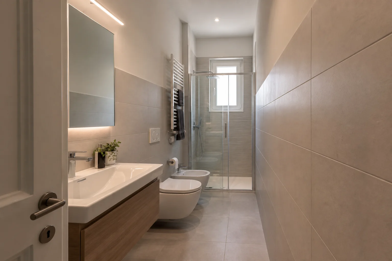 Bagno lungo e stretto ristrutturato con passaggio centrale, sanitari in linea e doccia sul fondo